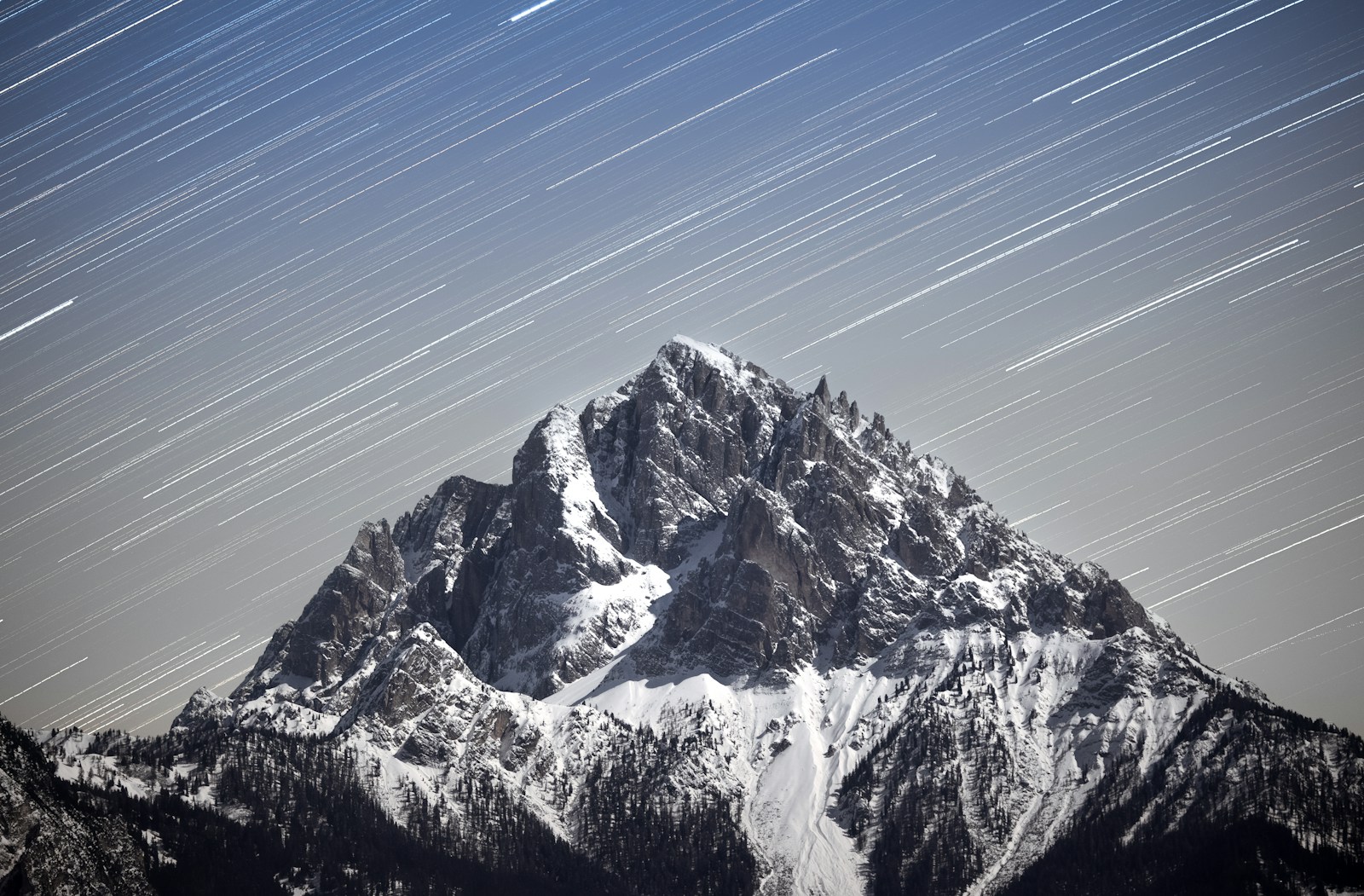 Snowy mountain peak under streaking stars